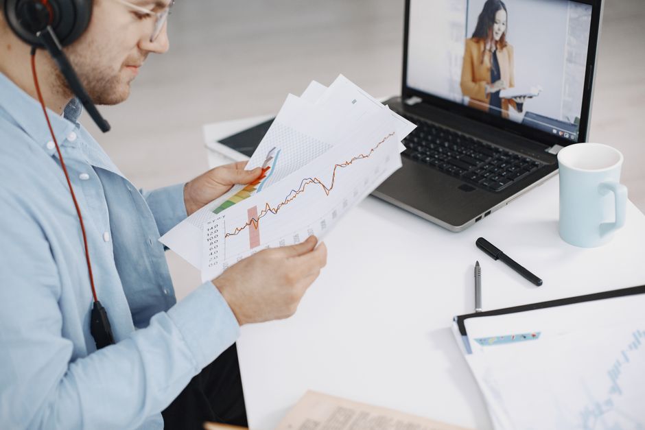 Business professional analyzing charts during a remote meeting with video call and headset.