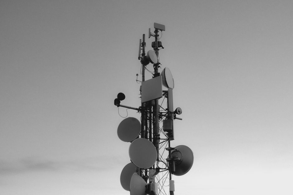 Monochrome image of a tall communications tower with satellite dishes under an expansive sky.