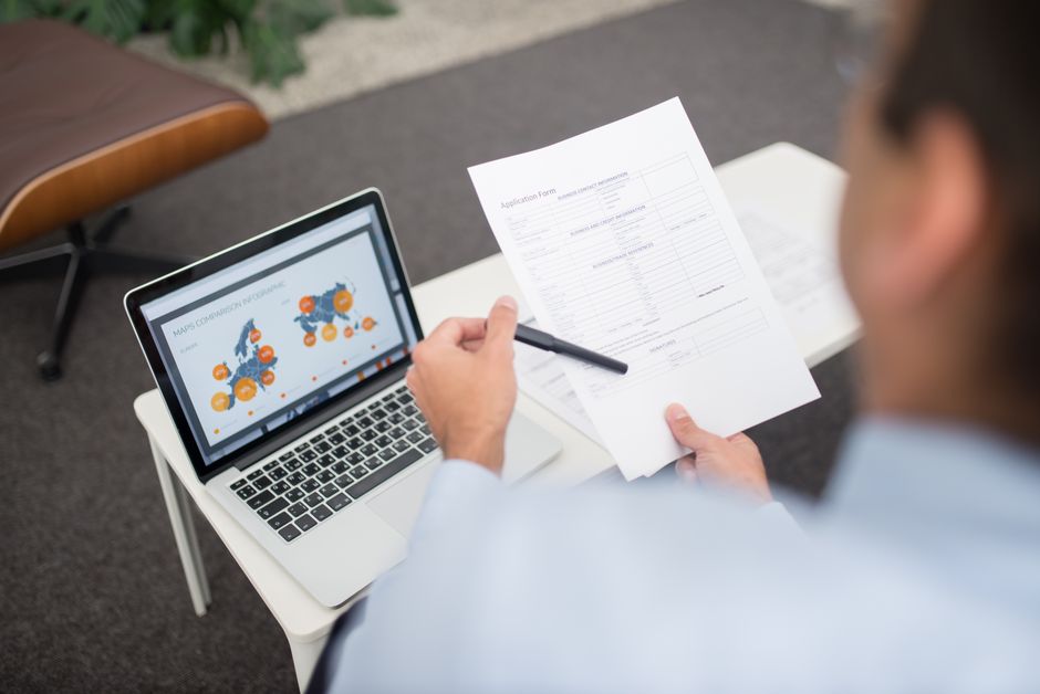 Professional setting with businessman reviewing documents and data on a laptop in an office.