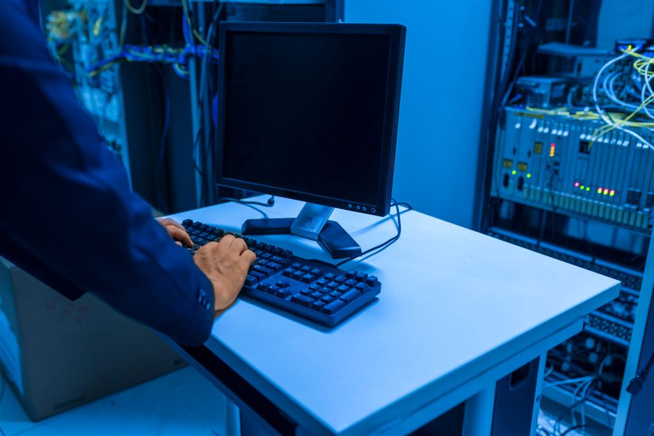 An IT professional operates a computer in a server room, managing network systems and connected devices.