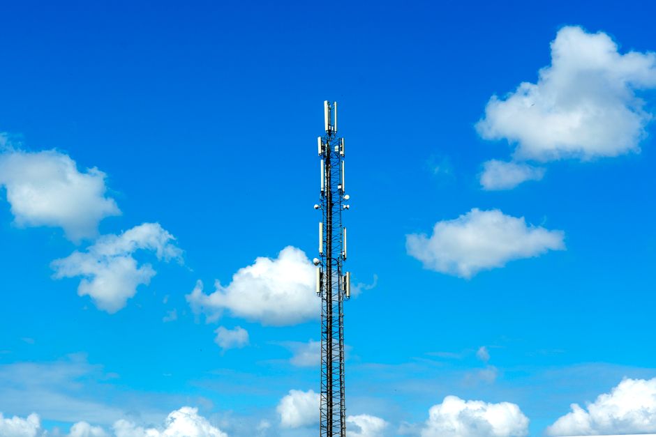 A radio tower standing tall against a vibrant blue sky dotted with fluffy clouds, showcasing telecommunication infrastructure.