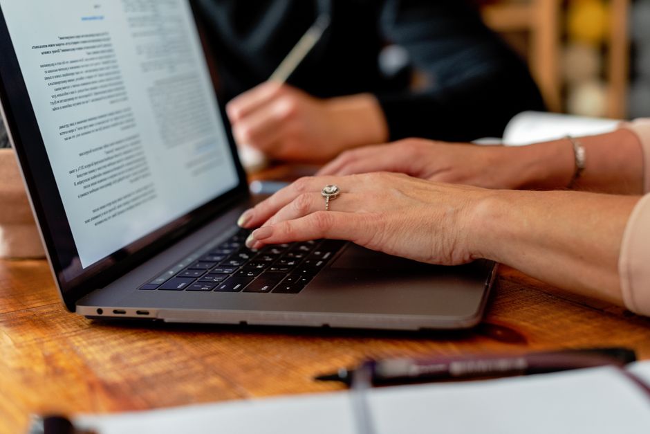 Adult hands with jewelry typing on a laptop in a professional indoor environment.