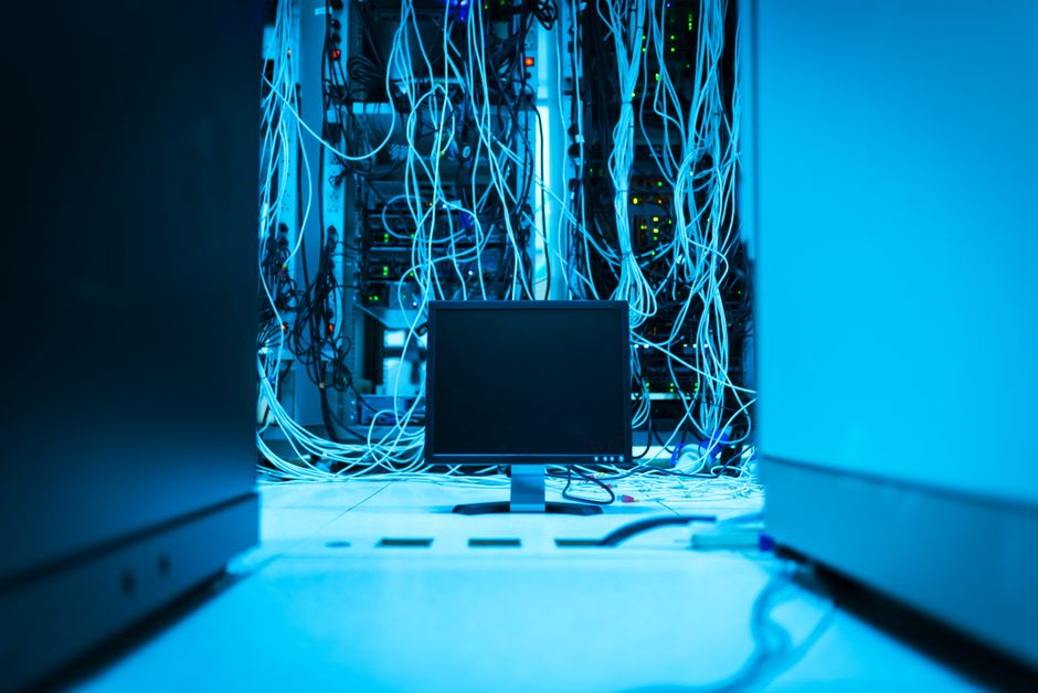 A complex network of cables in a data center with a monitor in the foreground.